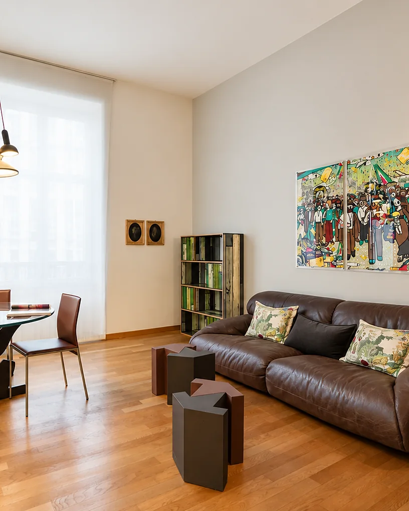 Soggiorno con un divano in pelle, un tavolo da pranzo sotto un lampadario a grappolo e un quadro colorato alla parete: Casa Garibaldi, Milano