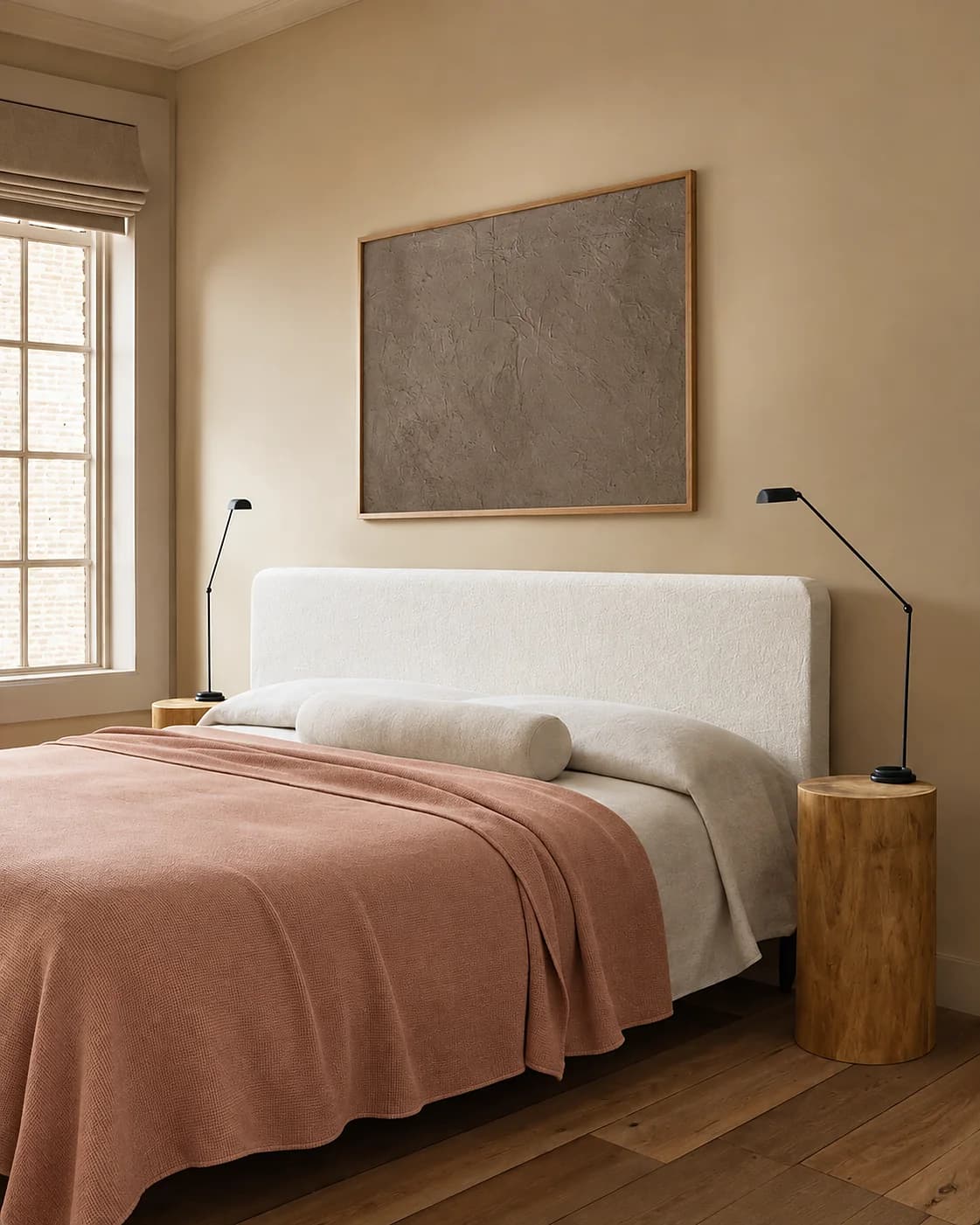 A bedroom with a dusty-pink throw, a wooden bedside table and a painting above the bed