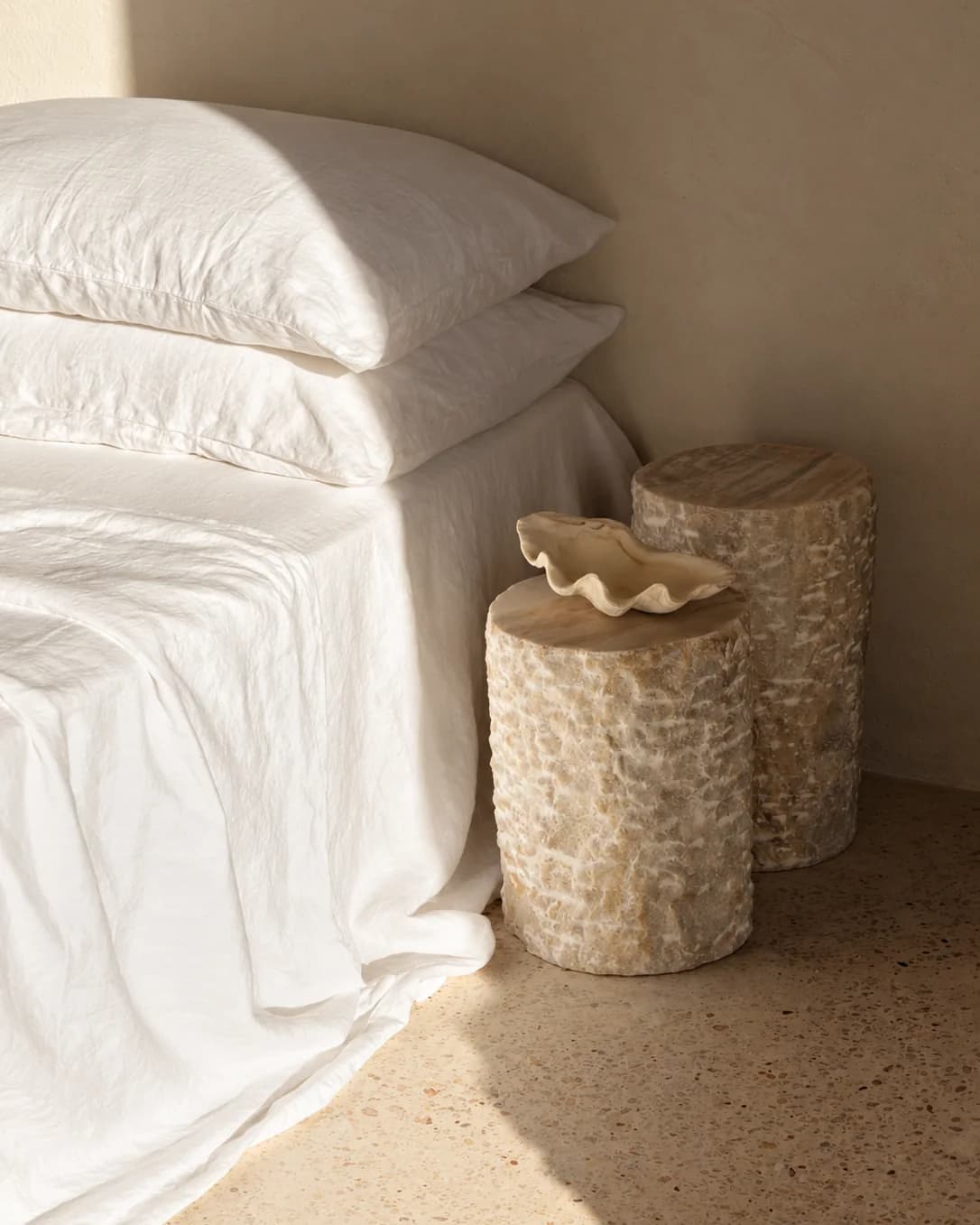 Un letto con le lenzuola di lino bianco e due sgabelli di pietra accanto