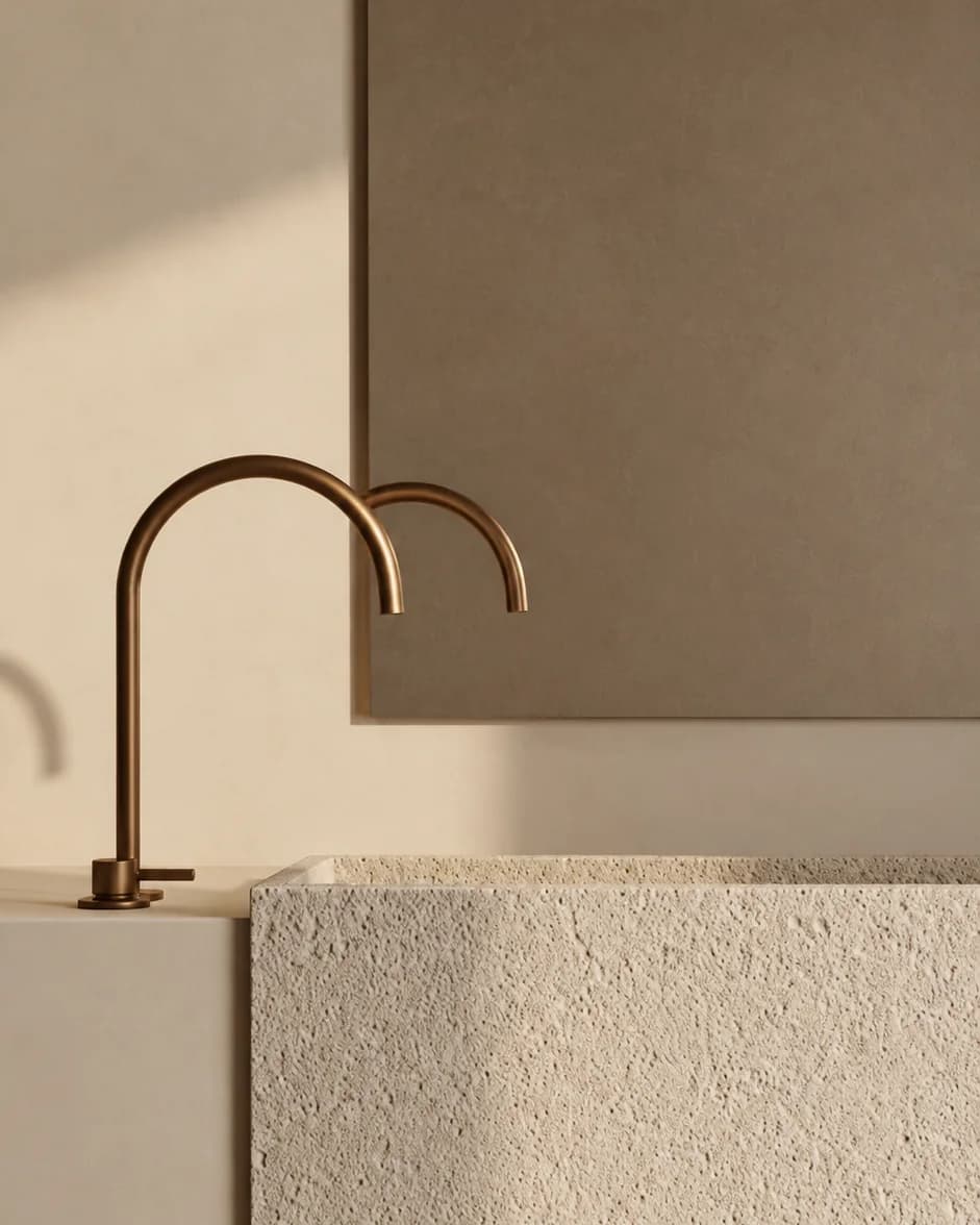 Un rubinetto di bronzo ad arco su un lavabo di pietra chiara, riflesso in uno specchio