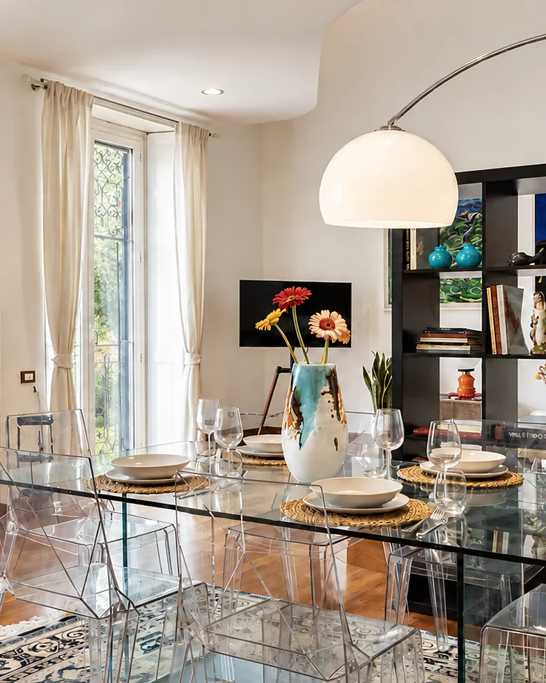 Glass table laid under an arc lamp, with a bookcase behind: Trastevere Art House, Rome