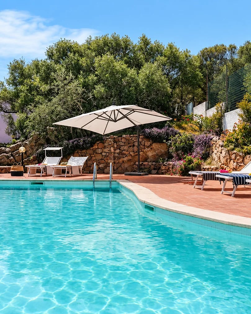 Pool with loungers and a parasol, in a garden with a stone wall: Villa Azzurra, Sardinia