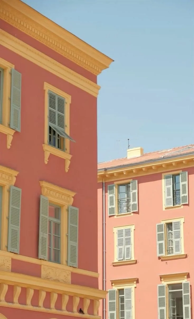 La facciata rosa di un palazzo genovese, con le persiane verdi e gialle e una balaustra di pietra