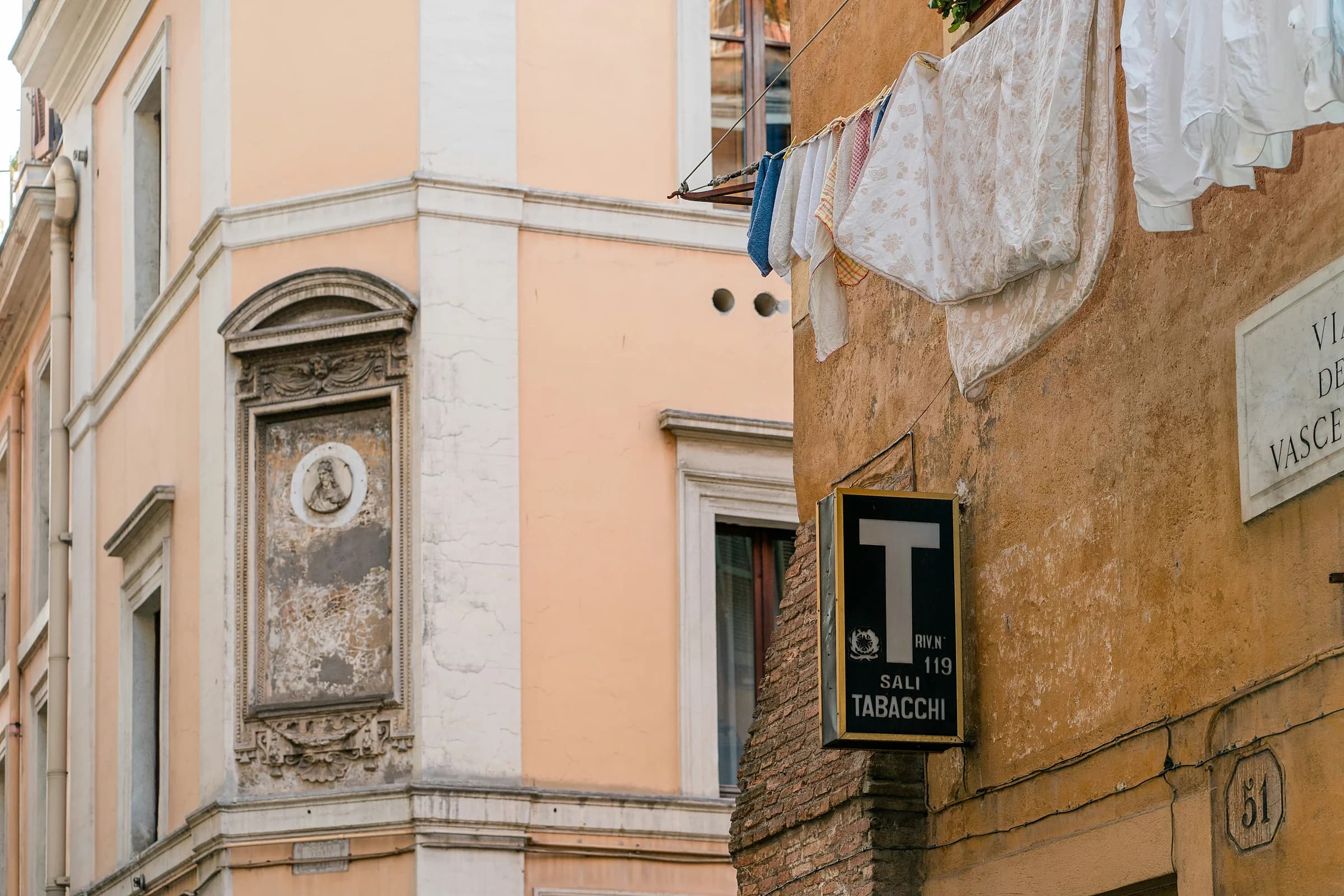 L’angolo di una via con un palazzo giallo, l’insegna della tabaccheria e una lapide di marmo