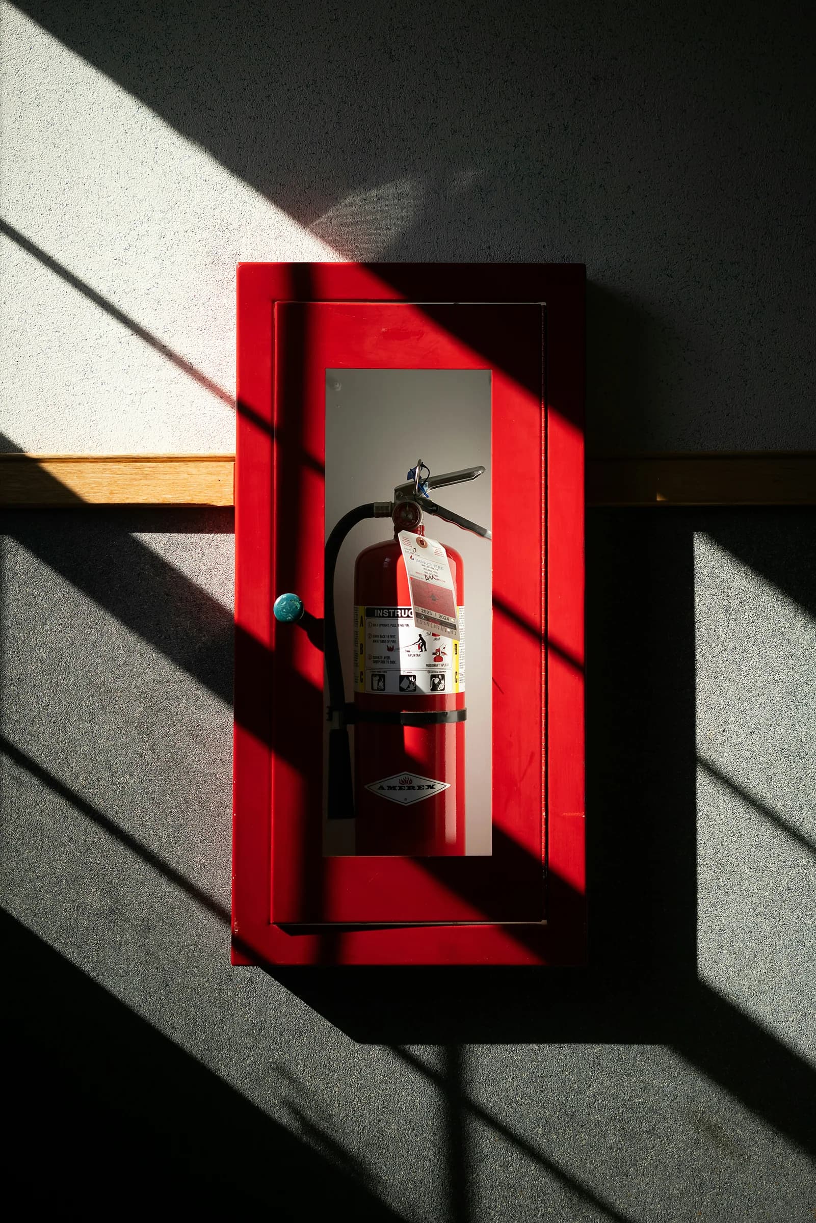 Un estintore dentro la sua cassetta rossa a muro, nella luce di taglio del pomeriggio