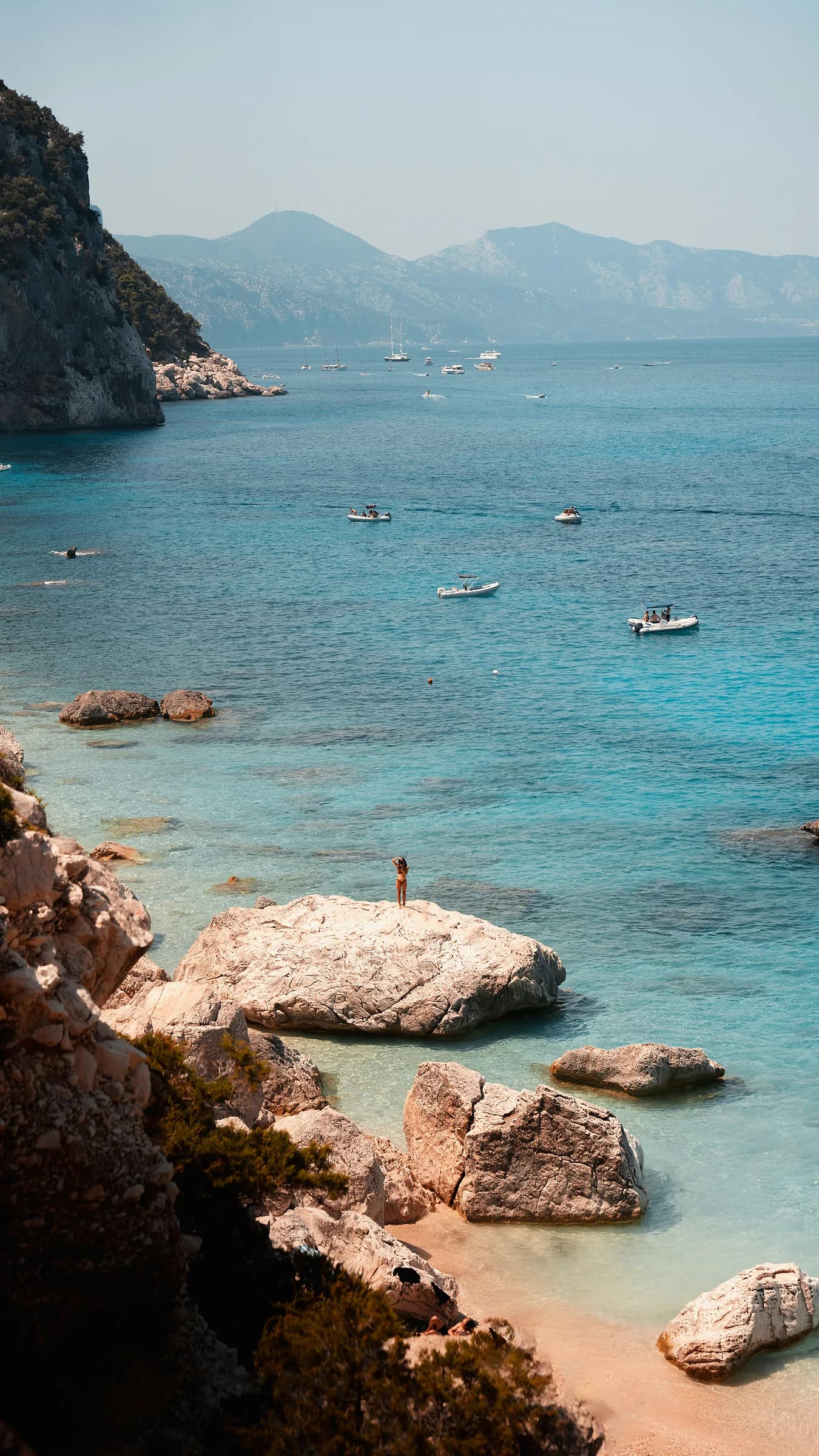 Una cala dall’acqua turchese con gli scogli affioranti e qualche barca all’ancora