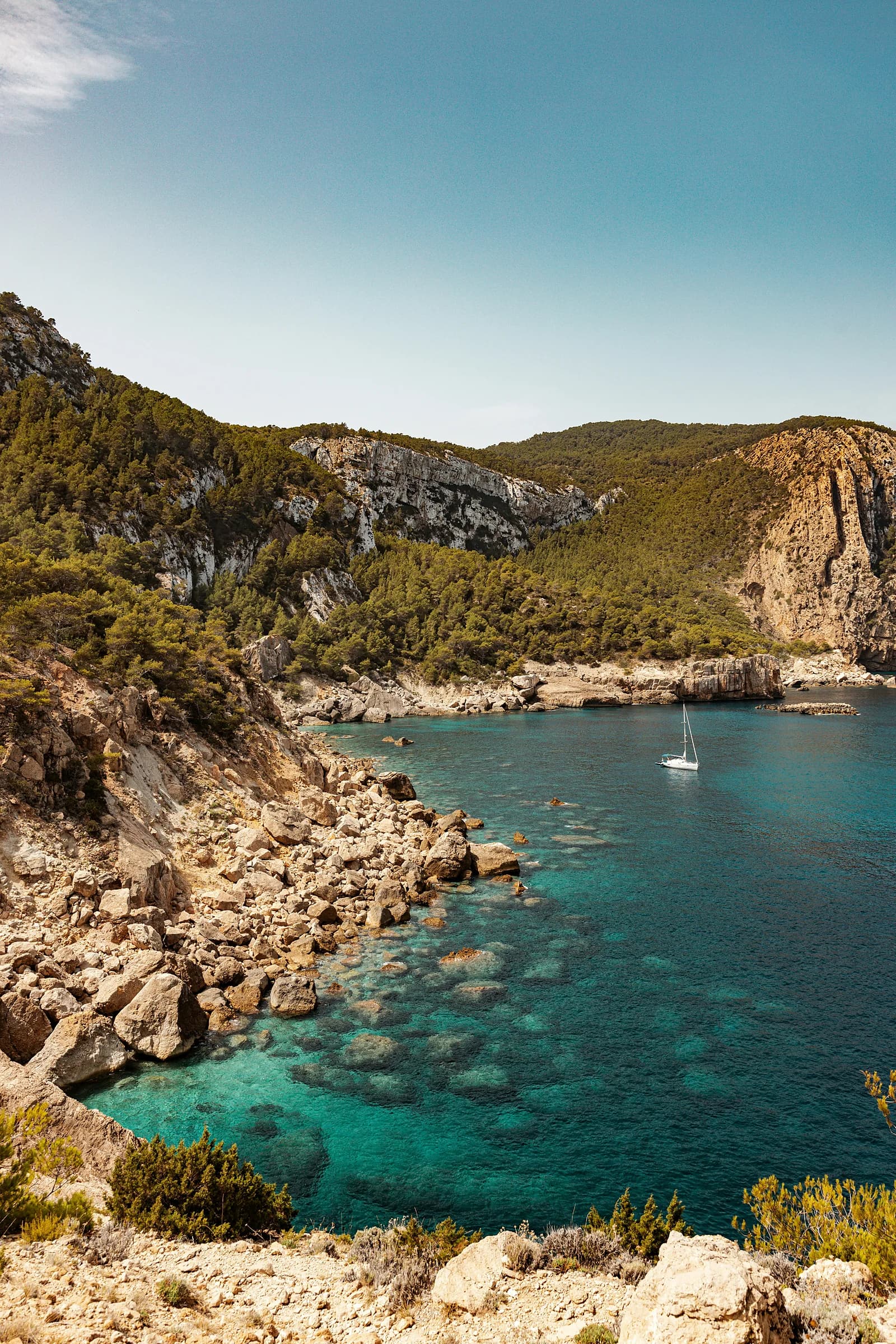 Una cala dall’acqua turchese fra gli scogli e la macchia, con una barca all’ancora