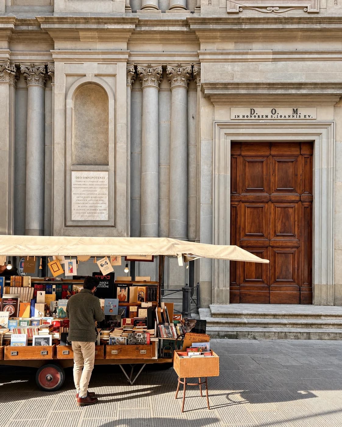 Una bancarella di libri davanti a una chiesa con le colonne, e una persona che sfoglia