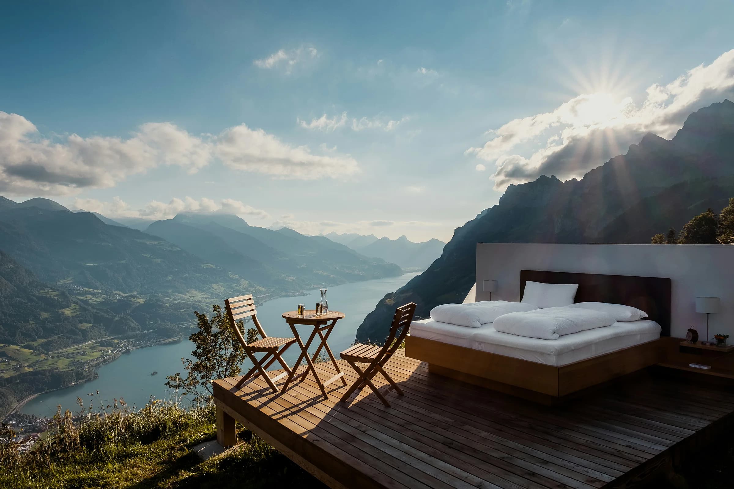 Un letto su una pedana di legno affacciata sul lago e sulle montagne, nella luce del mattino
