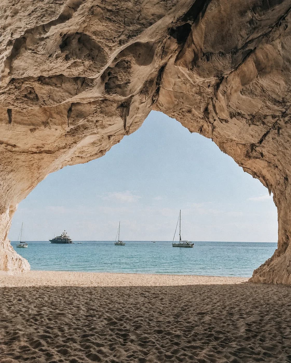 A rock arch over the sea, with boats at anchor, in Sardinia