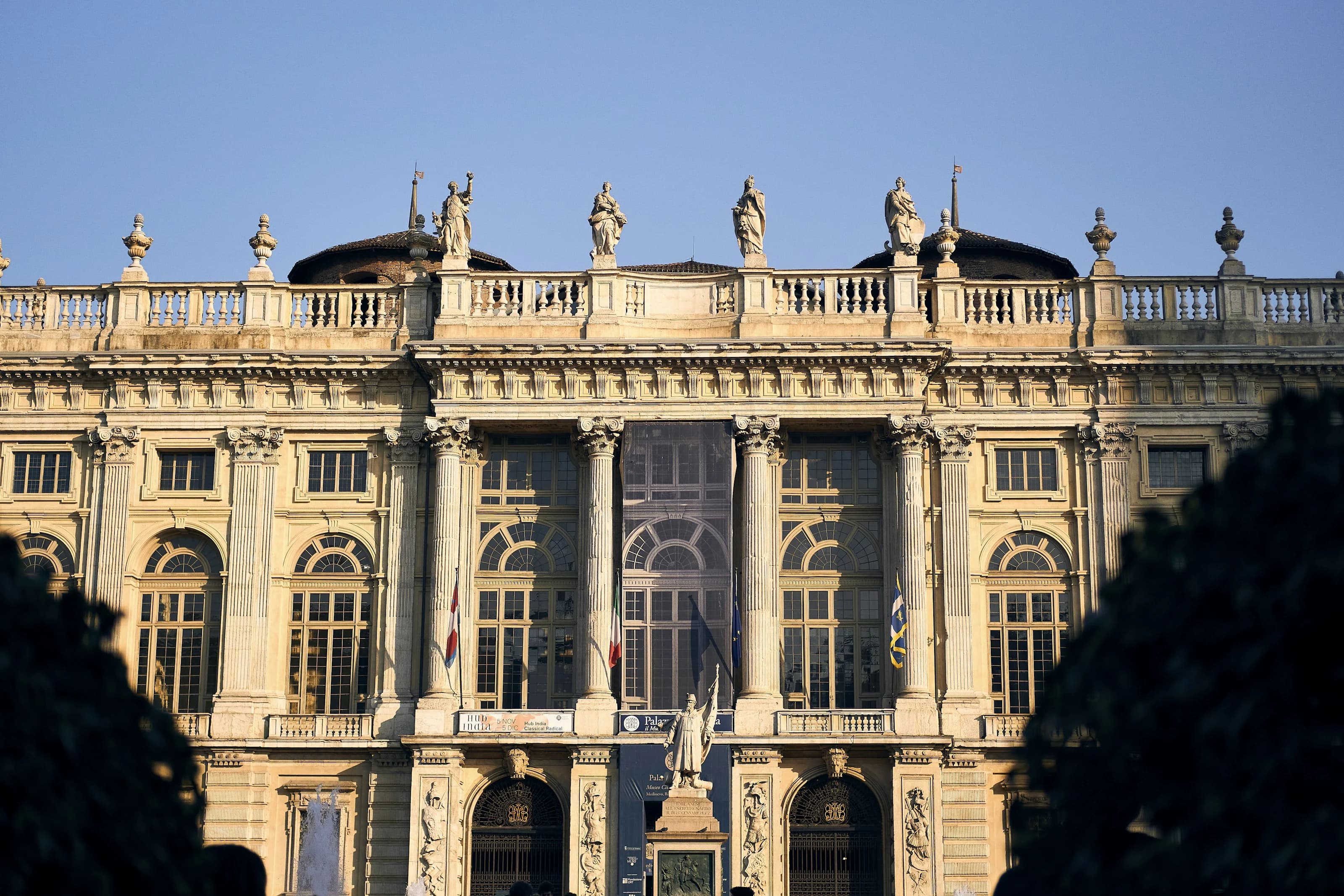 The Baroque façade of Palazzo Madama in Turin in the late-afternoon sun: tall columns, arched windows and statues along the balustrade, against a clear sky