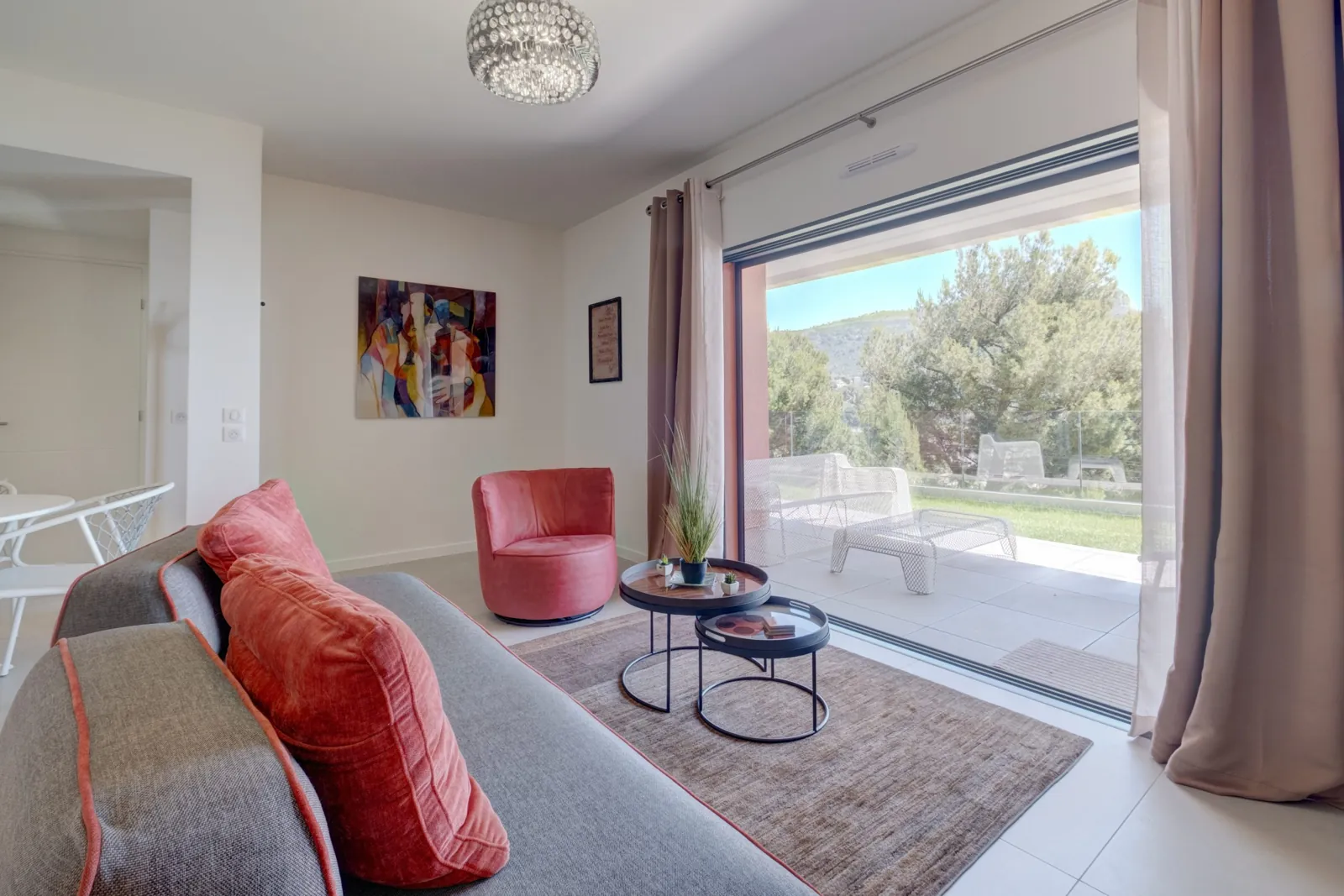 The living room of Incanto Luxe Apartment: a grey sofa, a pink armchair and the glass door open onto the garden