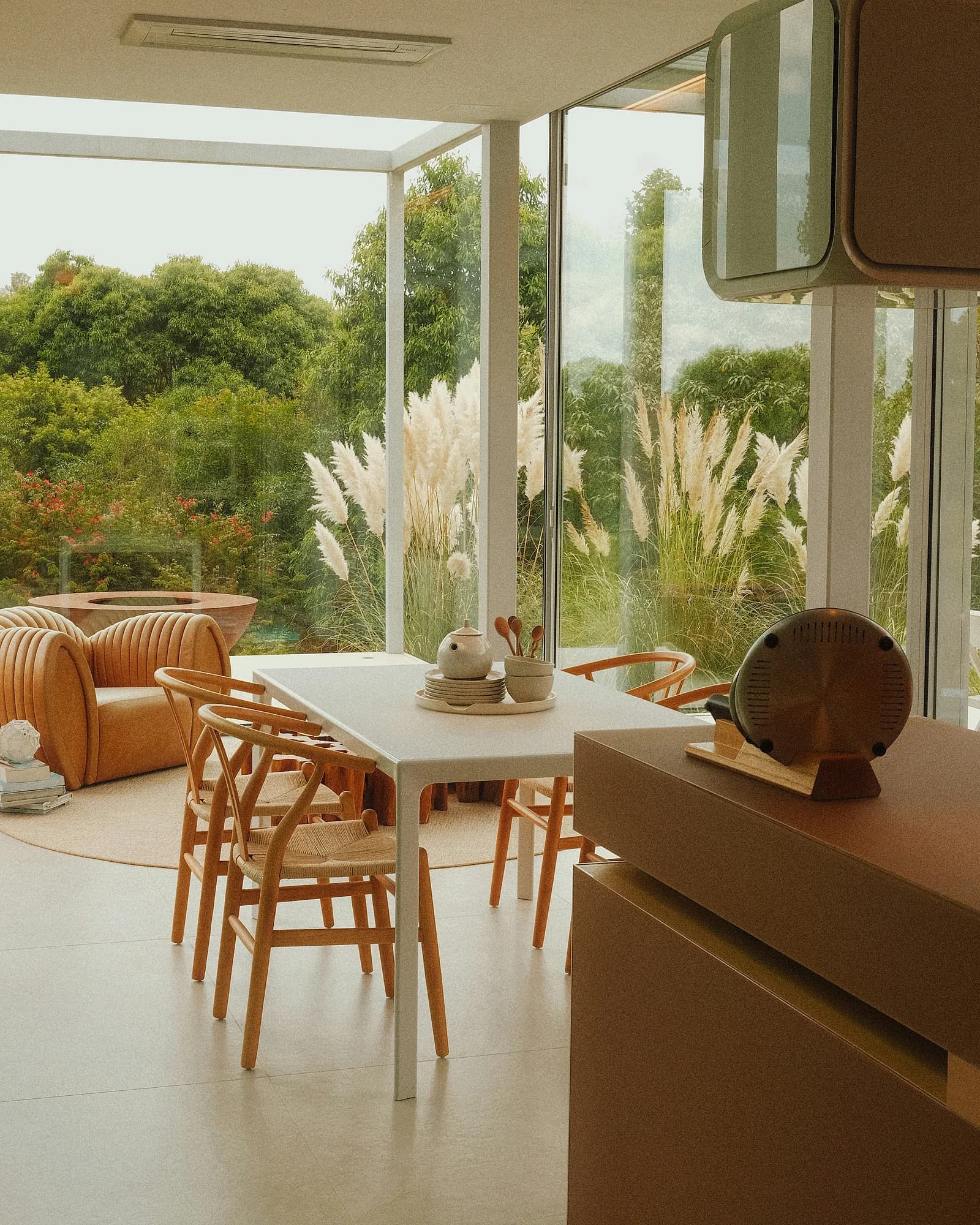 A bright dining room with a long table and wooden chairs, in front of the window onto the garden