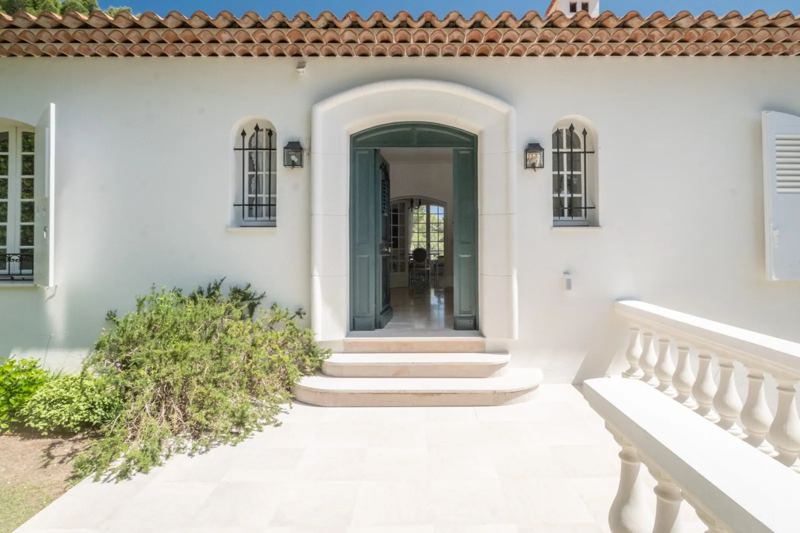 An open green front door in a white house with a tiled roof, a lantern on each side, stone steps and a white balustrade